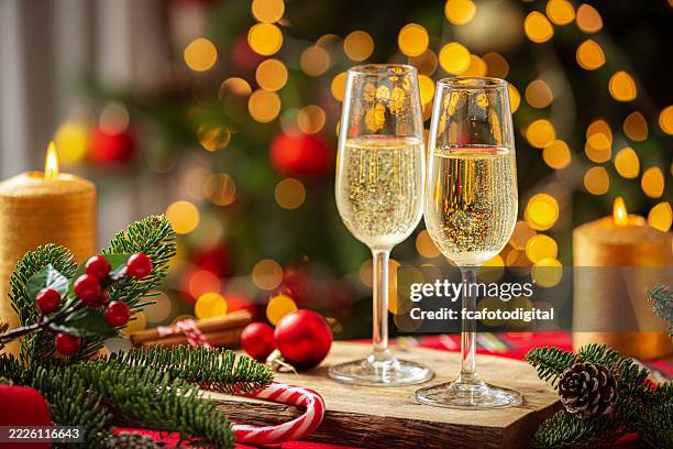 champagne flutes on christmas dining table. toast or holiday celebration. burning candles, candy cane and fit tree decor. defocused christmas tree and lights - champanhe imagens e fotografias de stock
