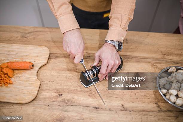an unrecognizable man sharpens a kitchen knife at the kitchen counter - sharpening stock pictures, royalty-free photos & images