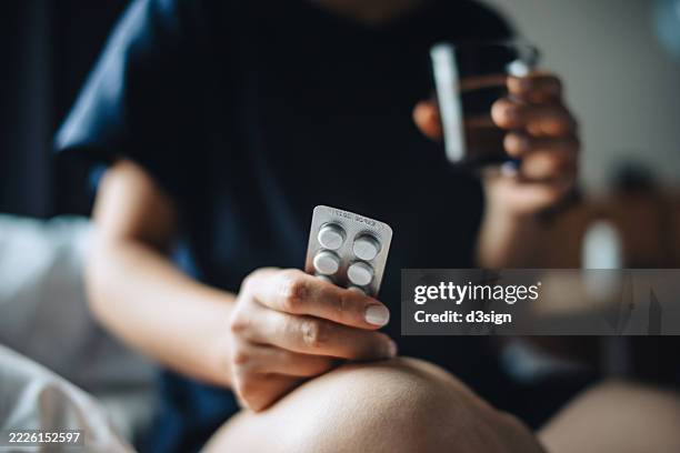 cropped shot of asian woman taking medicines with a glass of water at home. feeling sick. patient. medicines, antibiotics, healthcare, supplements and wellbeing concepts - schmerzmittel stock-fotos und bilder