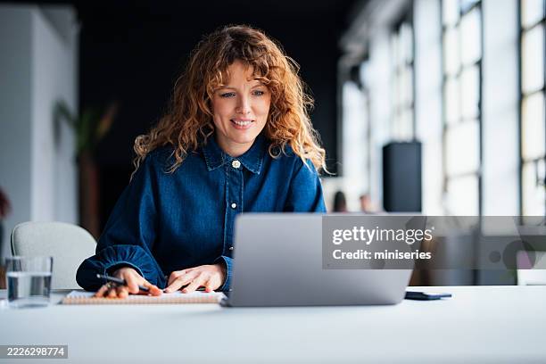 weibliche mitarbeiterin, die in einer modernen büroumgebung am laptop arbeitet - selbstversorgung stock-fotos und bilder