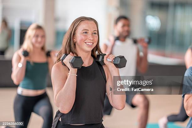group strength training class with participants holding dumbbells in a gym setting - lichaamsbeweging stockfoto's en -beelden