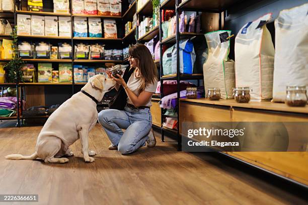 giovane donna che fa shopping con il suo cane in un moderno negozio di animali, scegliendo insieme forniture per animali domestici e cibo per cani. proprietario di animali domestici felice che si lega con il suo cane una visita casuale al negozio di animal - pet food foto e immagini stock