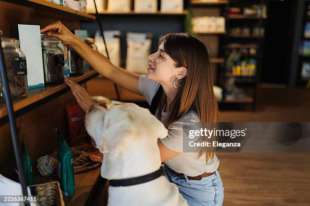 young woman shopping with her dog in a modern pet store, choosing pet supplies and dog food together. happy pet owner bonding with her dog a casual visit to the pet shop. - pet shop stock pictures, royalty-free photos & images