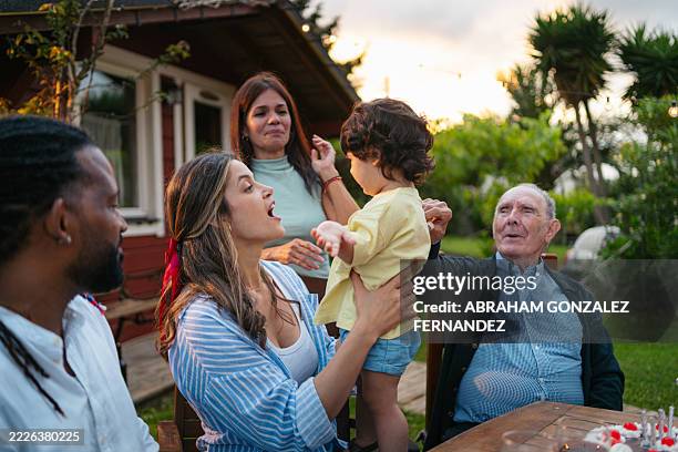 una familia multiétnica, incluido un niño pequeño, se reúne para una alegre celebración en su patio trasero - familia multigeneracional fotografías e imágenes de stock
