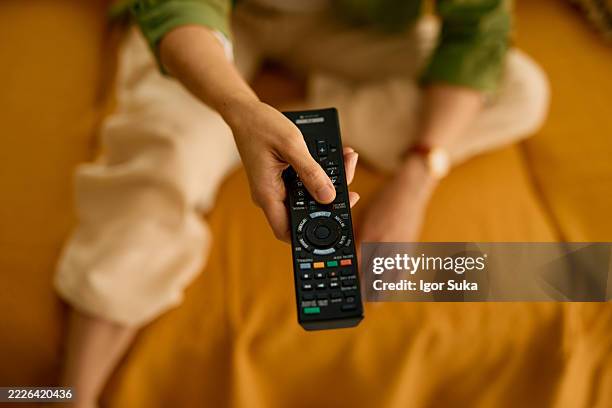 woman holding a sony tv remote control while sitting on a yellow sofa - remote control stock pictures, royalty-free photos & images
