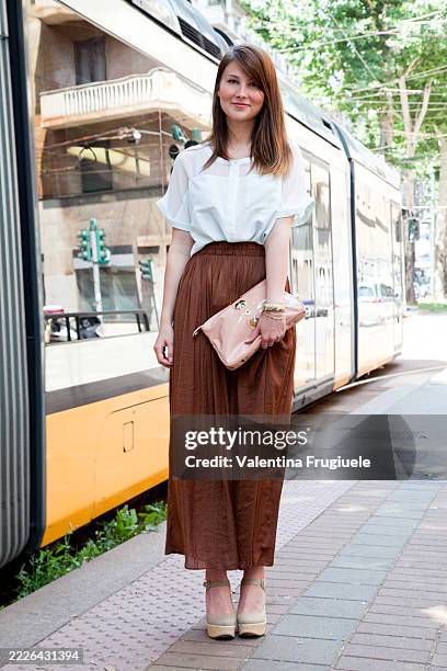 Angelica Ardasheva wears a pale blue blouse and chestnut pleated maxi skirt carried a blush patent clutch, exuding minimalist grace with beige...