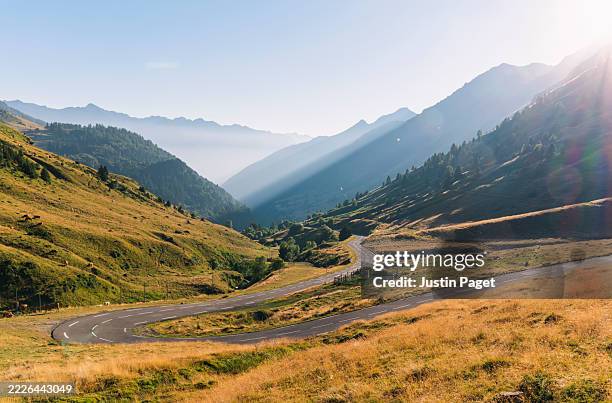 a beautiful landscape view down the valley to the west of the col du tourmalet in the french pyrenees mountains. the road snakes up through the valley - col de montagne photos et images de collection