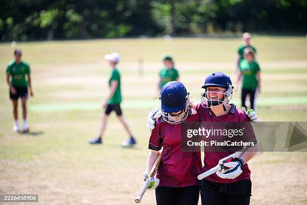 middle aged female batting pair walking off cricket field arms around shoulders after a successful game - cricket team stock pictures, royalty-free photos & images