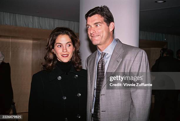 American actress Jami Gertz, wearing a black double-breasted coat, and her husband, American businessman Tony Ressler, who wears a grey blazer over a...