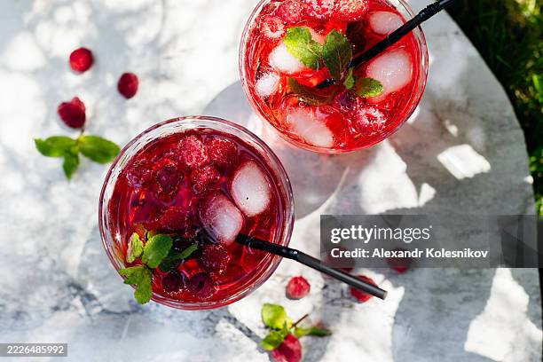 red raspberry lemonade with ice cube and mint leaf. gin, cocktail, ice tea, soda drink on light table in garden - raspberry cocktail stock pictures, royalty-free photos & images