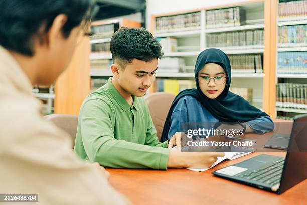 two asian student discussing on library and writing on their book - hijab back stock pictures, royalty-free photos & images