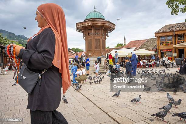 a woman wearing a hijab crosses sarajevo's main square, which is also known as baščaršija on a busy day - sarajevo stock pictures, royalty-free photos & images