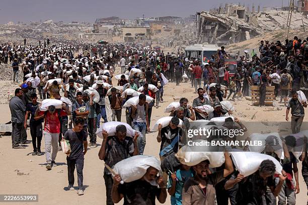 People walk with sacks of flour delivered after trucks carrying humanitarian aid entered northern Gaza on July 27, 2025 coming from the Zikim border...