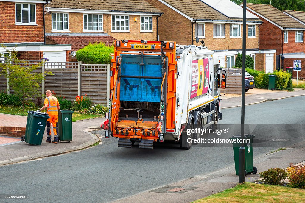 Waste collection worker putting rubbish bins back on residential driveway on city street