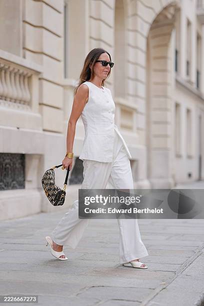 Alba Garavito Torre wears black rectangular Ray-Ban sunglasses, gold hoop earrings, a white sleeveless tailored top with structured front paneling...