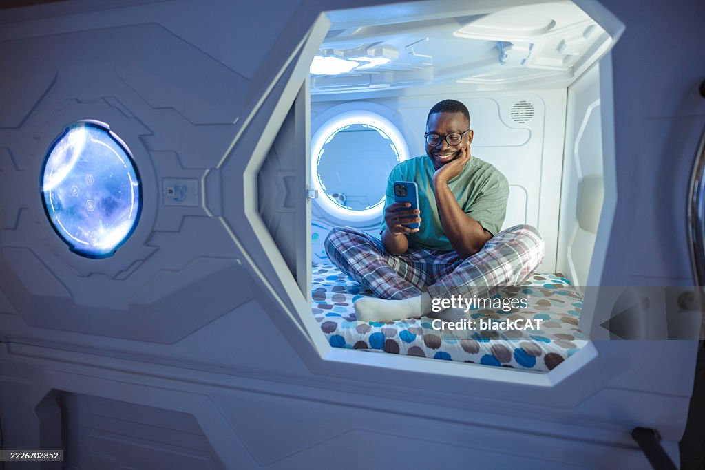 Man relaxing in modern pod accommodation while using smartphone