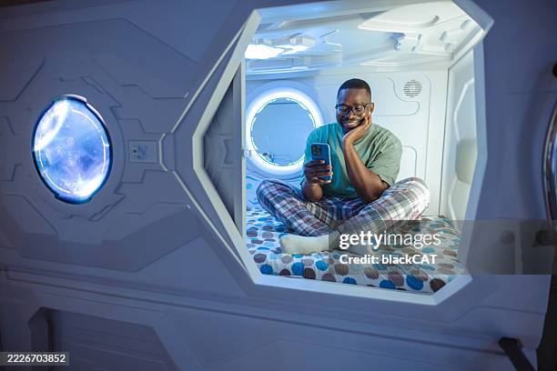 man relaxing in modern pod accommodation while using smartphone - capsule hotel stock pictures, royalty-free photos & images