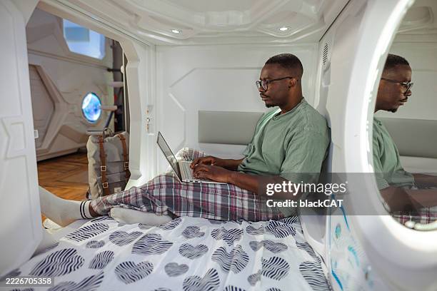 man relaxing with laptop inside a modern capsule room - nightwear stock pictures, royalty-free photos & images