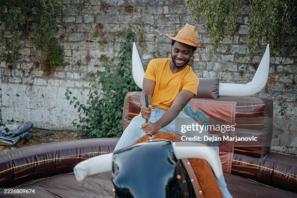 People Having Fun In The City Riding Mechanical Bull Outdoors High-Res Stock Photo