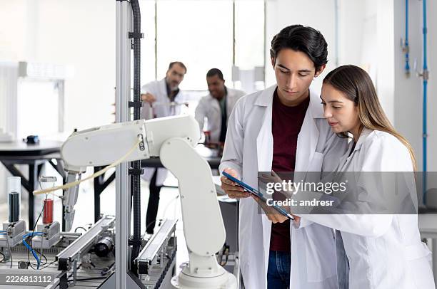 engineering students using a tablet while building a robotic arm in class - science and technology stock pictures, royalty-free photos & images