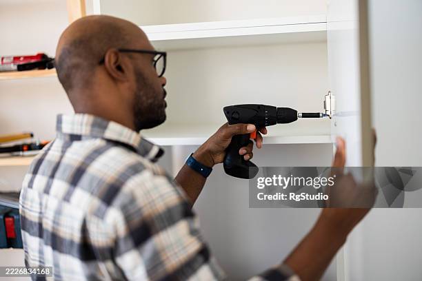 carpenter installing door hinge using cordless drill at home - black hinge stock pictures, royalty-free photos & images
