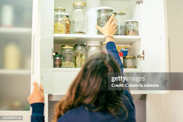 woman picking up jar of dried food from kitchen cabinet - voorraadkast stockfoto's en -beelden