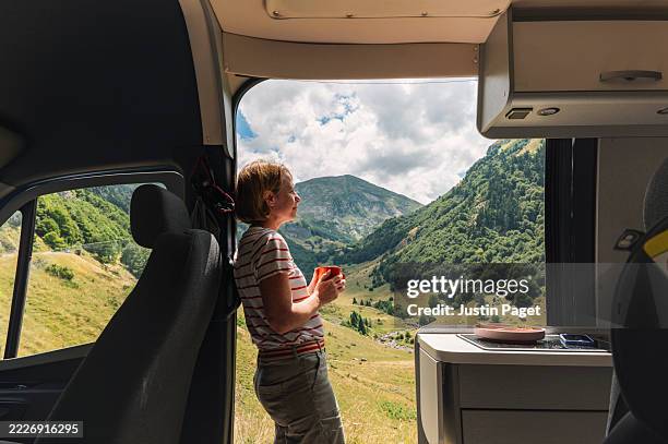 a mature woman takes in the valley view in the french pyrenees from her camper van - camping stock-fotos und bilder