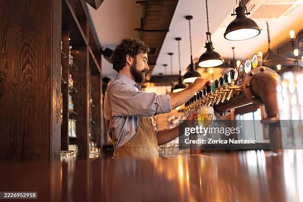 barkeeper schenkt frisches bier aus dem bierhahn ein - kneipe stock-fotos und bilder