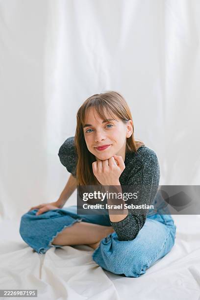 young woman sitting cross-legged and smiling at camera - hand on chin stock pictures, royalty-free photos & images