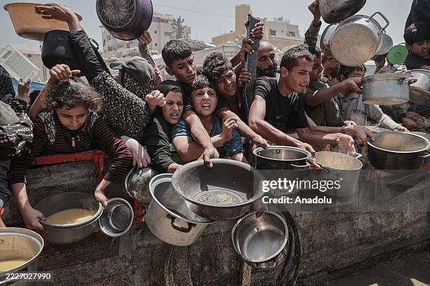 Palestinians, including children, who are struggling to access food due to Israel's blockade and ongoing attacks on the Gaza Strip, wait in line to...
