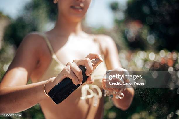 a 22-year-old young woman is seen outdoors applying sunscreen to her face under natural sunlight, capturing a moment of self-care and skin protection. - sonnenschutz stock-fotos und bilder