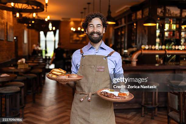 cheerful male server presenting tasty meals to guests - ober stockfoto's en -beelden