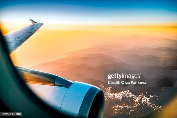 airplane wing flying over mountains at sunset, seen from passenger window - clouds from aircraft point of view stock pictures, royalty-free photos & images