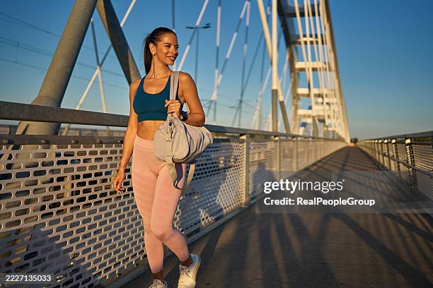 young athletic woman walking on a bridge after exercising - duffle bag stock pictures, royalty-free photos & images