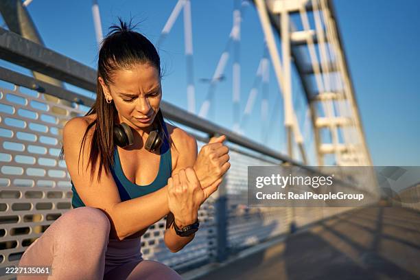 young sportswoman feeling wrist pain while exercising on bridge - wrist stock pictures, royalty-free photos & images