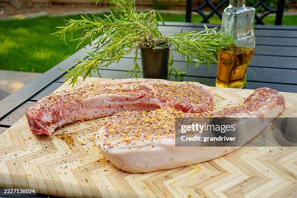 roh gewürzte schweinekoteletts auf einem schneidebrett mit rosmarin und öl in der nähe - schweinebauch stock-fotos und bilder