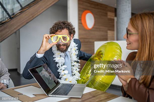businessman wearing diving mask and hawaiian lei holding inflatable ring in office - diving equipment stock pictures, royalty-free photos & images