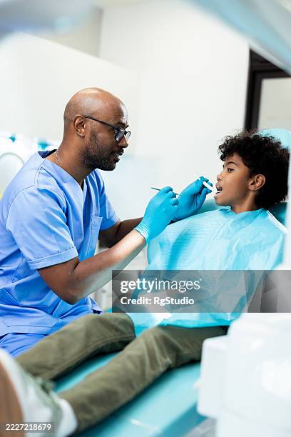 dentista masculino examinando los dientes de un niño en una clínica dental - odontopediatría fotografías e imágenes de stock