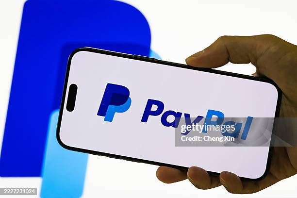 In this photo illustration, a person holds a smartphone displaying the logo of PayPal Holdings Inc. , a leading American financial technology company...