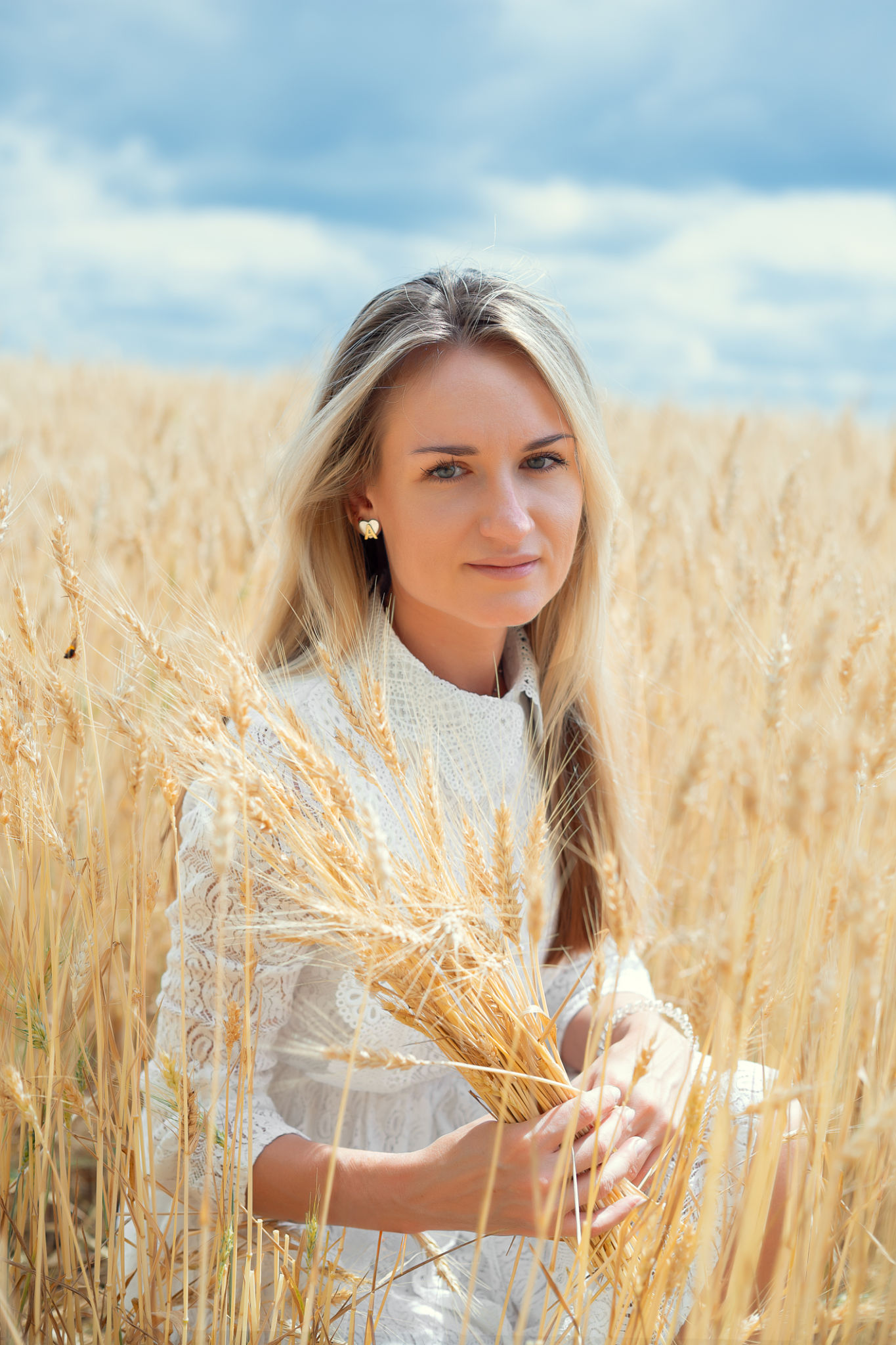 Young blonde woman holding wheat in a field under a cloudy sky Young blonde woman holding wheat in a field under a cloudy sky