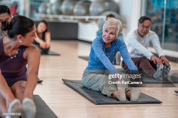 group yoga class with diverse individuals stretching on exercise mats - yoga class stock pictures, royalty-free photos & images