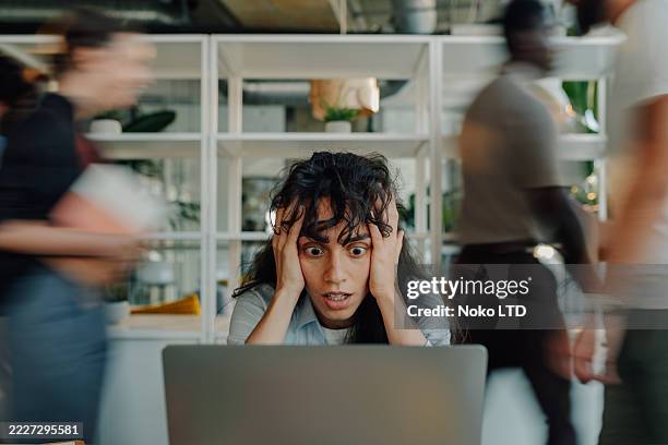 imprenditrice stressata che guarda il laptop con i colleghi che si precipitano in ufficio - caos foto e immagini stock