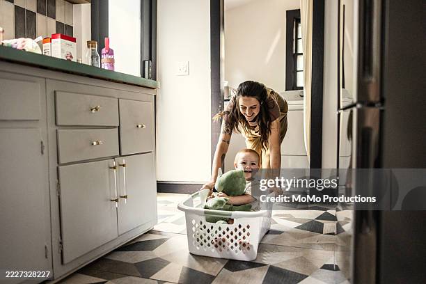 mother pushing young son through house in laundry basket - lessive corvée domestique photos et images de collection