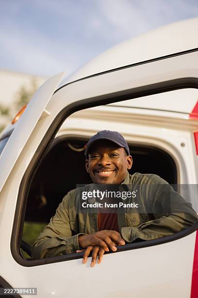 truck driver smiling from inside cabin of his delivery truck - vrachtwagenchauffeur stockfoto's en -beelden