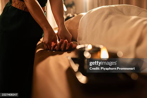 thailändischer therapeut, der eine handmassage mit warmem öl aus einer geschmolzenen massagekerze durchführt. sanftes licht und gemütliche spa-einrichtung schaffen eine ruhige, therapeutische wellness-atmosphäre. - aromaöl stock-fotos und bilder