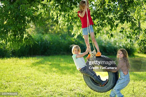 children playing on a tree swing in a sunny backyard setting - backyard swing stock pictures, royalty-free photos & images