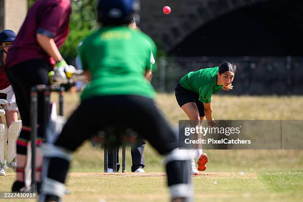 joven jugadora de bolos enfocada mirando la pelota con el bateador y el wicketkeeper en primer plano - equipo de críquet fotografías e imágenes de stock