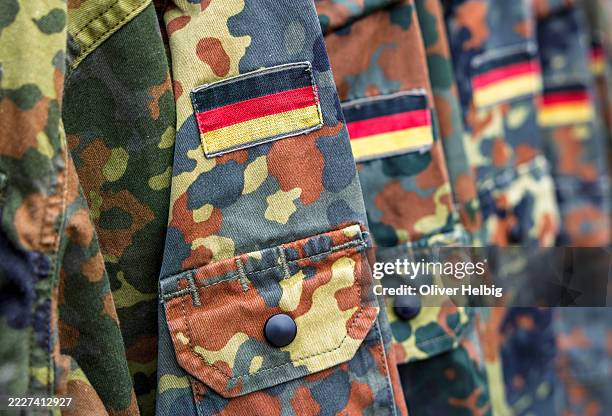 german military uniforms hanging with flecktarn camouflage pattern and flag - duitse leger stockfoto's en -beelden