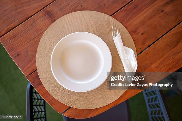 empty white plate with fork and napkin on wooden table - tischset stock-fotos und bilder