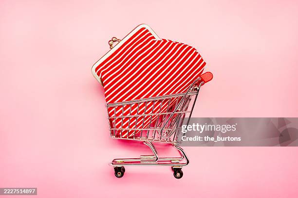 high angle view of a small shopping cart and red change purse on pink background - winkelwagentje stockfoto's en -beelden